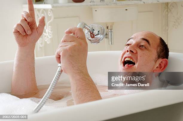 man lying in bath singing into shower head, close-up - singing shower stock pictures, royalty-free photos & images