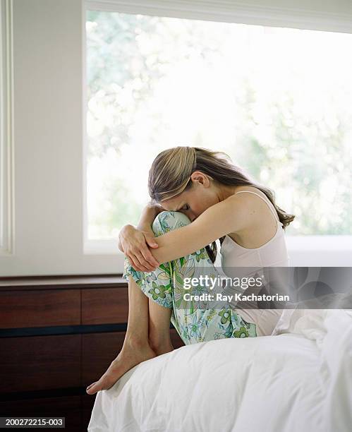 woman sitting on edge of bed, resting head on legs, side view - hugging knees stock pictures, royalty-free photos & images