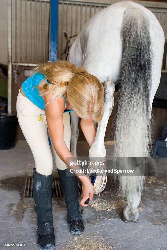 Teenage girl (16-18) cleaning horse's hoof