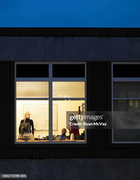 three young businesspeople in office, view through window, night - businessman distance window ストックフォトと画像