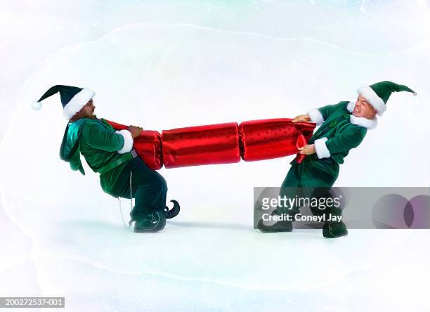 two male 'elves' pulling large christmas cracker (digital enhancement) - elfe stock-fotos und bilder