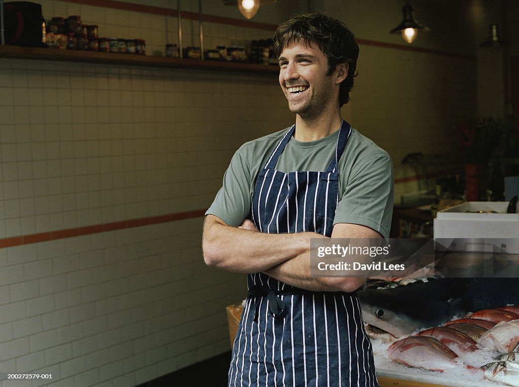 Male fishmonger standing by counter, arms folded, smiling