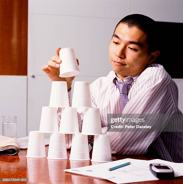young businessman at desk building up plastic cups - perder el tiempo fotografías e imágenes de stock