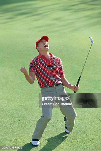 male golfer celebrating on green, holding up club, eyes closed - golfer stock pictures, royalty-free photos & images