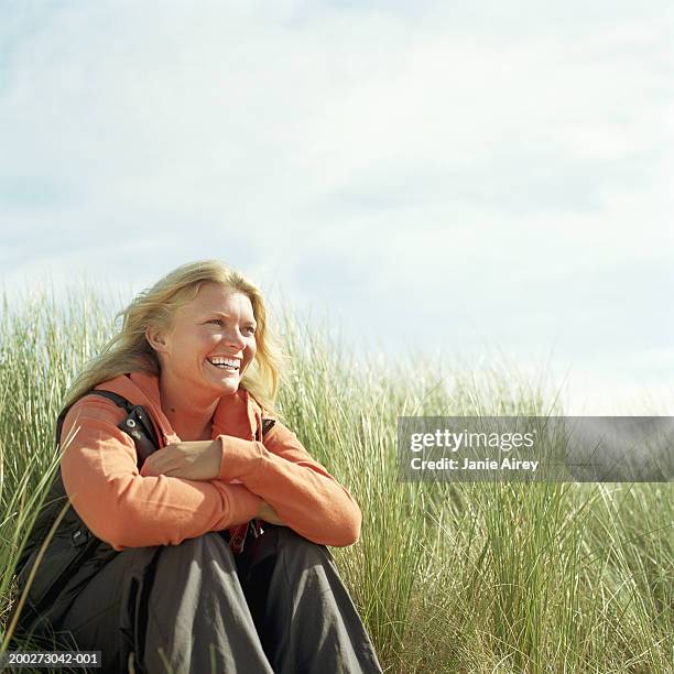 young woman sitting amongst tall grass, smiling - tall blonde women stock pictures, royalty-free photos & images