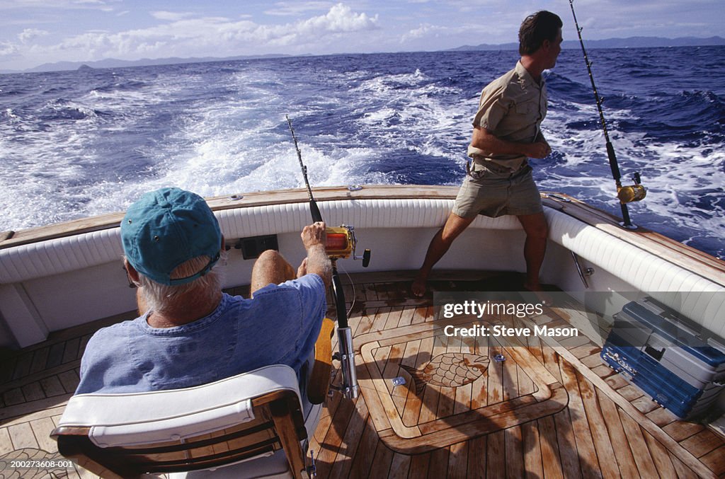 Two Men Fishing On Deck Of Boat Man Looking At Ocean High-Res