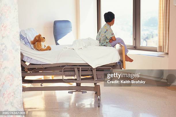 young boy (6-7) sitting on hospital bed - boy sitting on bed stock-fotos und bilder