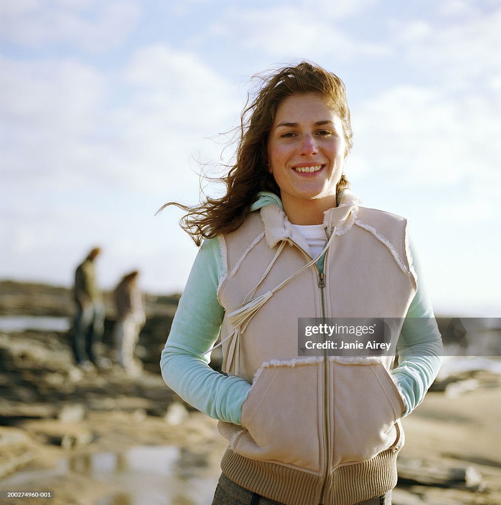 Young woman standing on beach, smiling, portrait