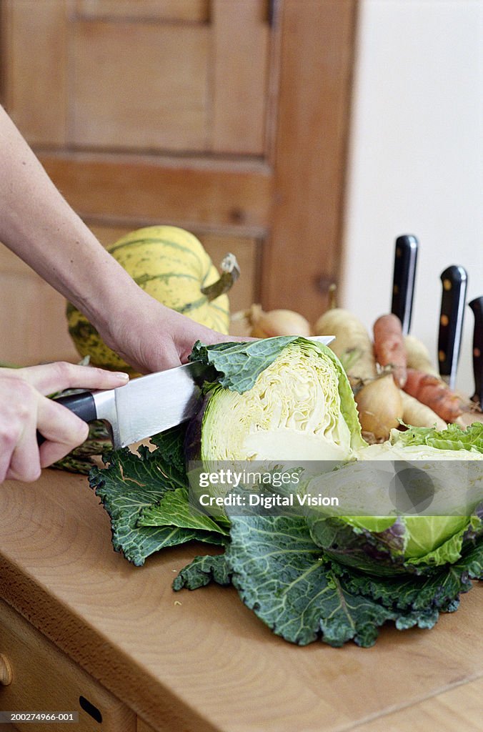 Woman in kitchen slicing savoy cabbage, close-up of hands