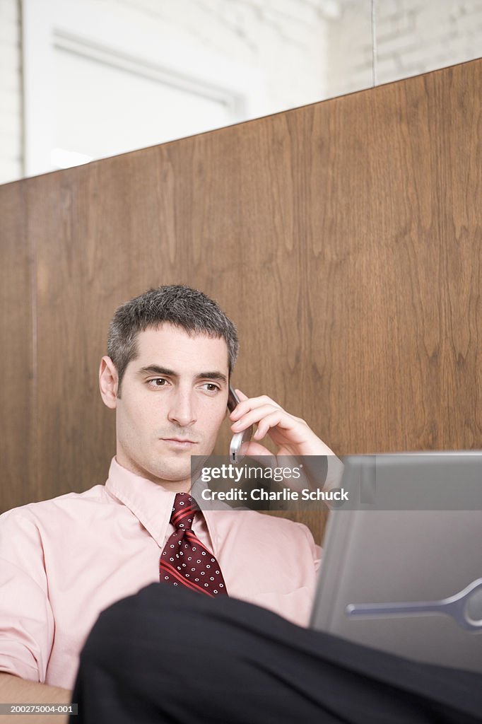 Young businessman using mobile phone and laptop computer