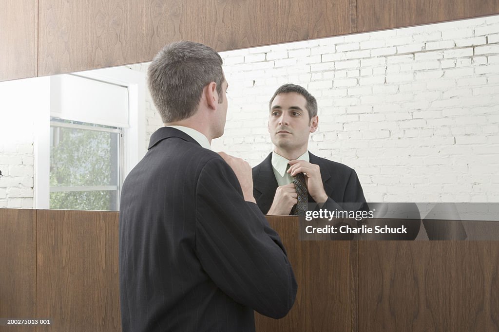 Young businessman adjusting tie in mirror