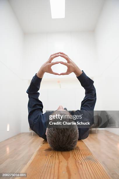 man lying on bench with arms raised, fingertips pressed together - parte superior de la cabeza fotografías e imágenes de stock