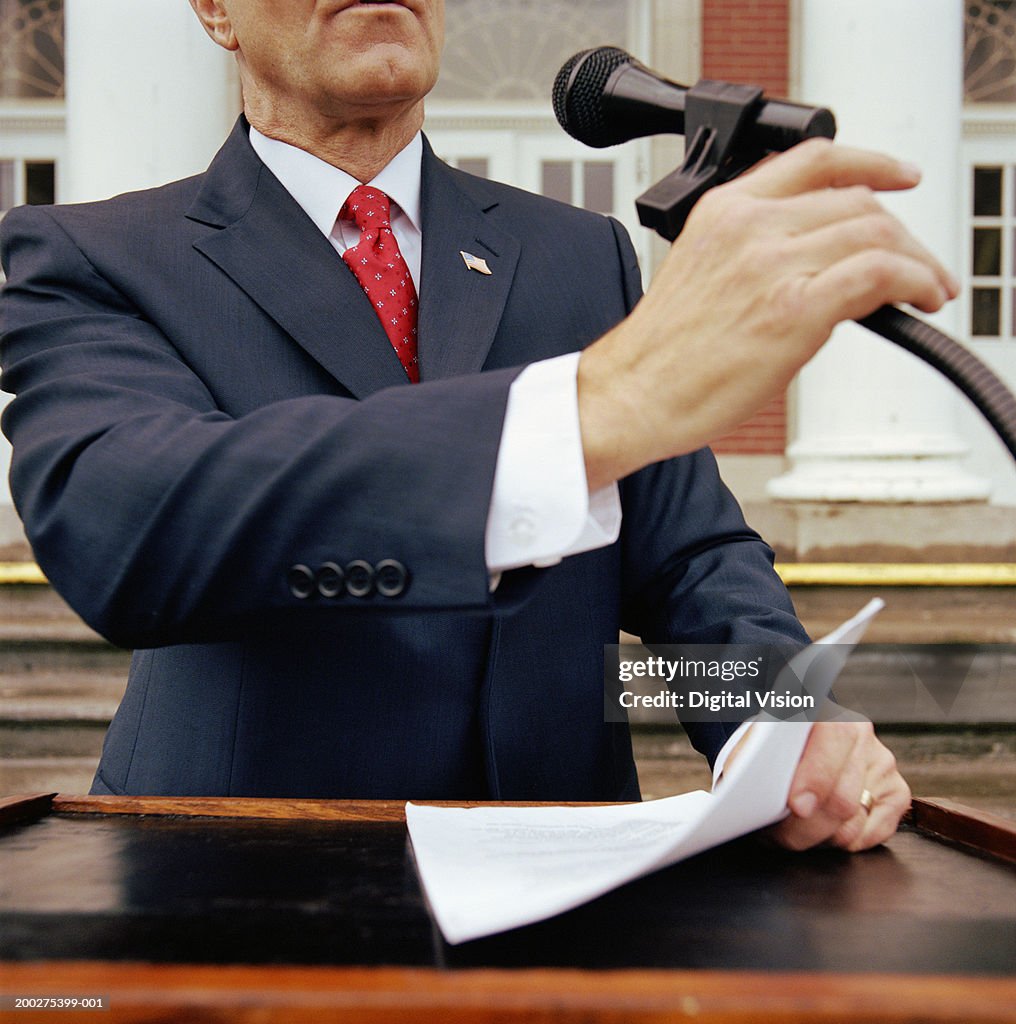 Mature Businessman at lectern outdoors, holding microphone and documents