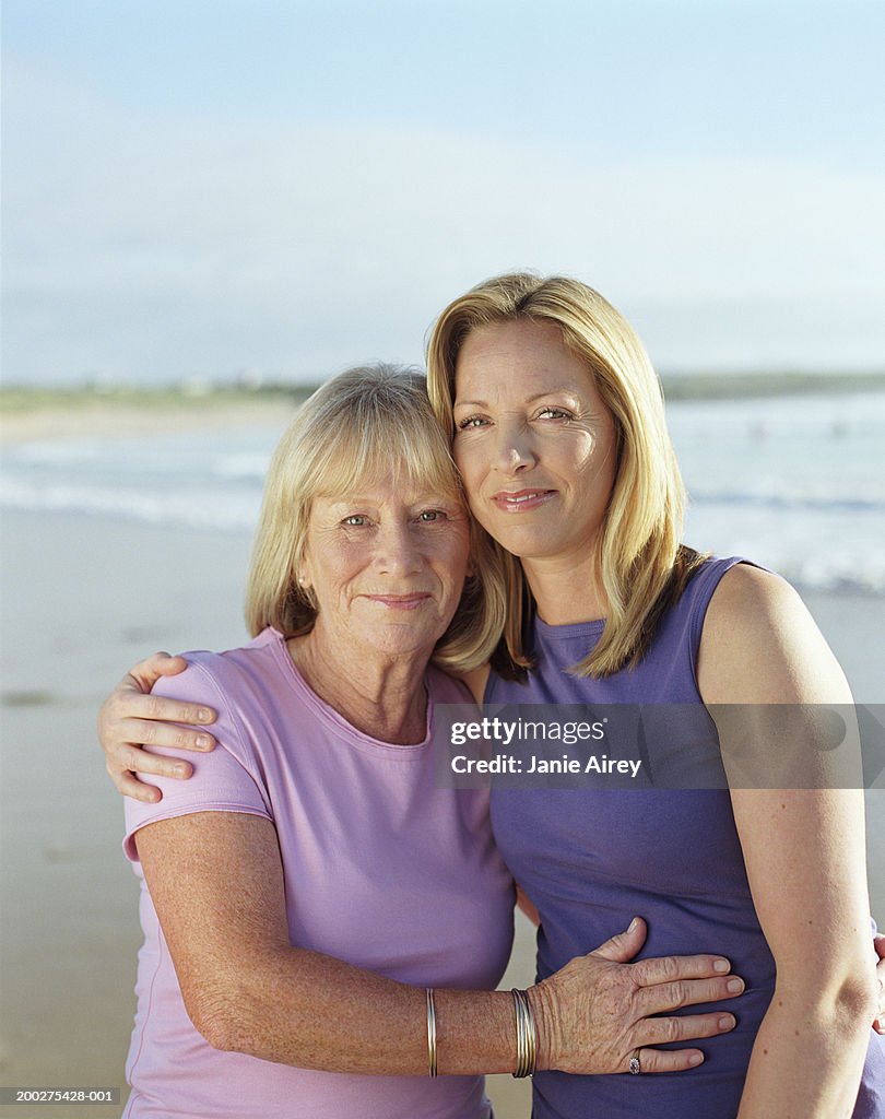 Mother and mature daughter embracing on beach, smiling, portrait