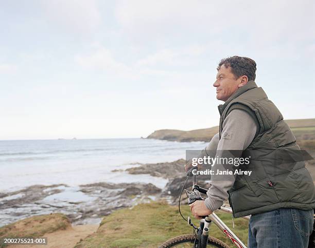 mature man holding bicycle handle bars, overlooking sea, side view - man side view stock pictures, royalty-free photos & images