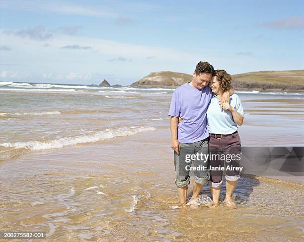 mature couple embracing, standing in water on beach, smiling - knöcheltief im wasser stock-fotos und bilder