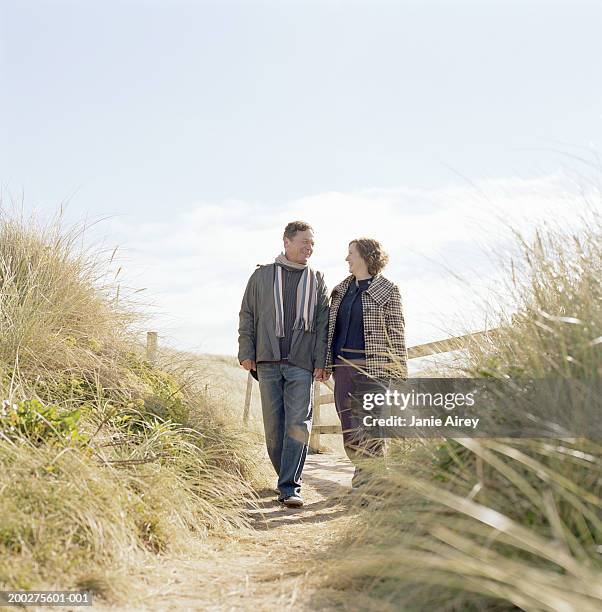 mature couple walking on path through sand dunes, smiling - couple dunes stock pictures, royalty-free photos & images