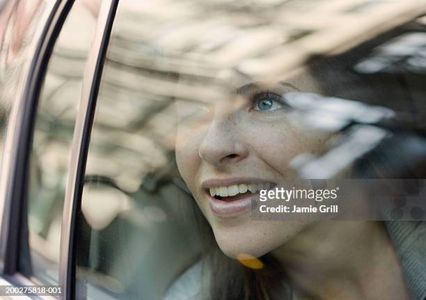 young woman looking out of car window, smiling - awe stockfoto's en -beelden