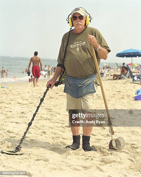 mature man on beach with metal detector, portrait - schatzoeken stockfoto's en -beelden