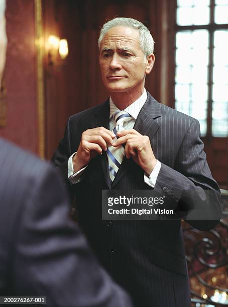 mature businessman adjusting tie, reflection in mirror - man reflection foto e immagini stock