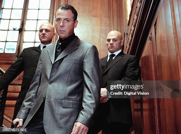 mature businessman flanked by two security guards in panelled room, portrait - criminal stock-fotos und bilder