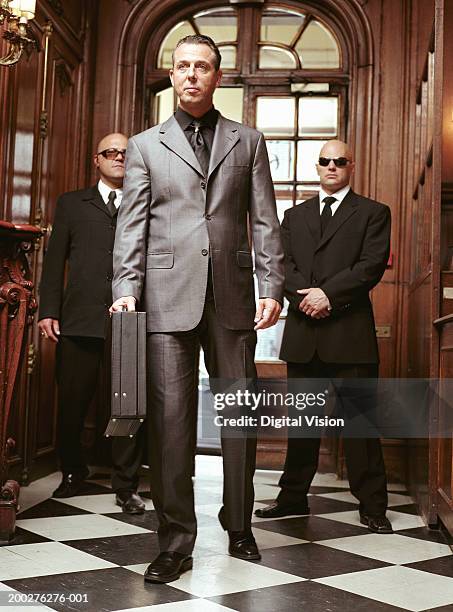 mature businessman entering hallway, two security guards standing behind - banden stock-fotos und bilder