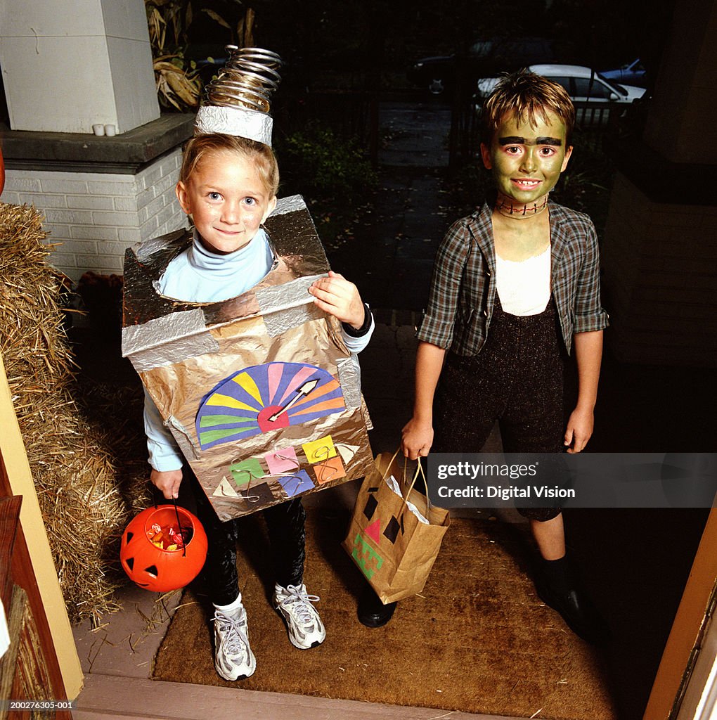 Girl (4-6) and boy (7-9) in costumes standing on doorstep, portrait