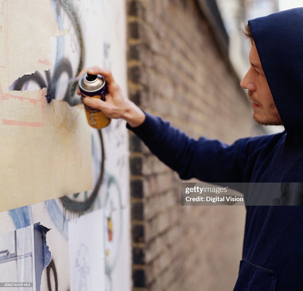 Young man wearing hooded top, spraying graffiti on wall, side view