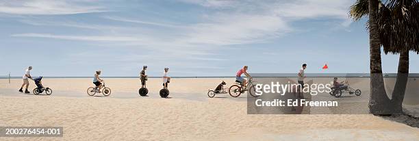 people riding bikes, roller skating on beach (digital composite) - suit photos et images de collection