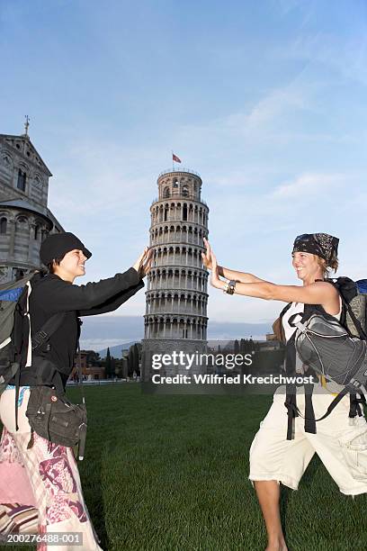 italy, pisa, two women pretending to hold up the leaning tower of pisa - perspectiva forzada fotografías e imágenes de stock