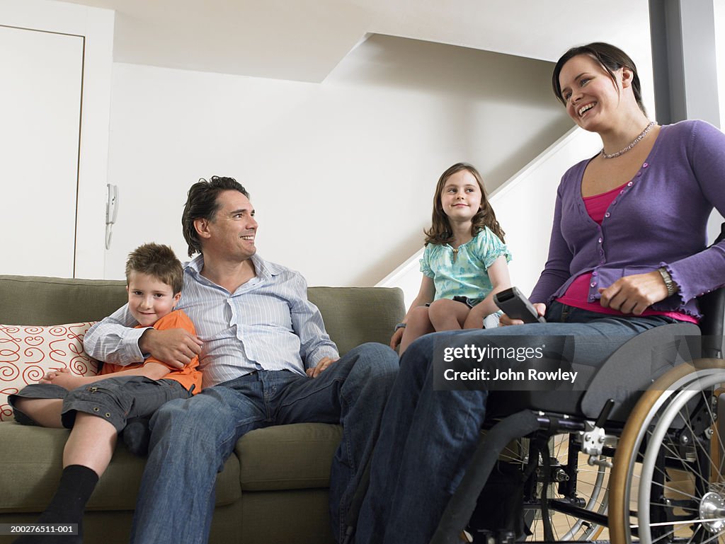 Parents relaxing in living room with son and daughter (7-9) woman in wheelchair, smiling