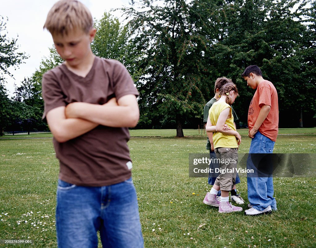 Children (9-12) standing in park, boy with arms crossed in foreground