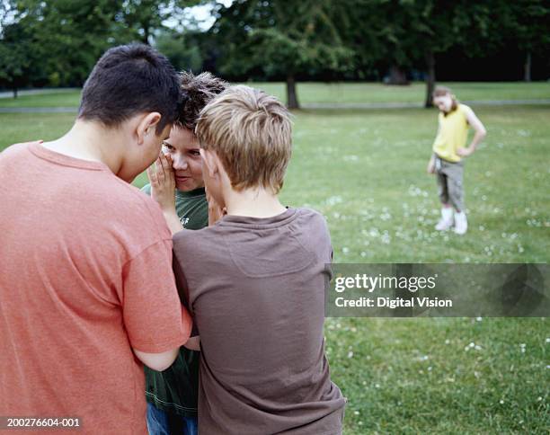 boys (9-12) in park whispering in huddle, girl (9-11) in background - mid distance stockfoto's en -beelden