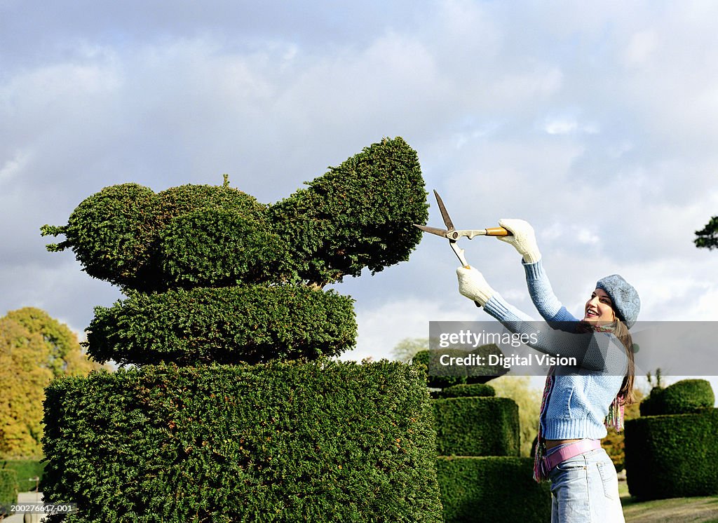 Young woman pruning hedge into shape of bird, side view