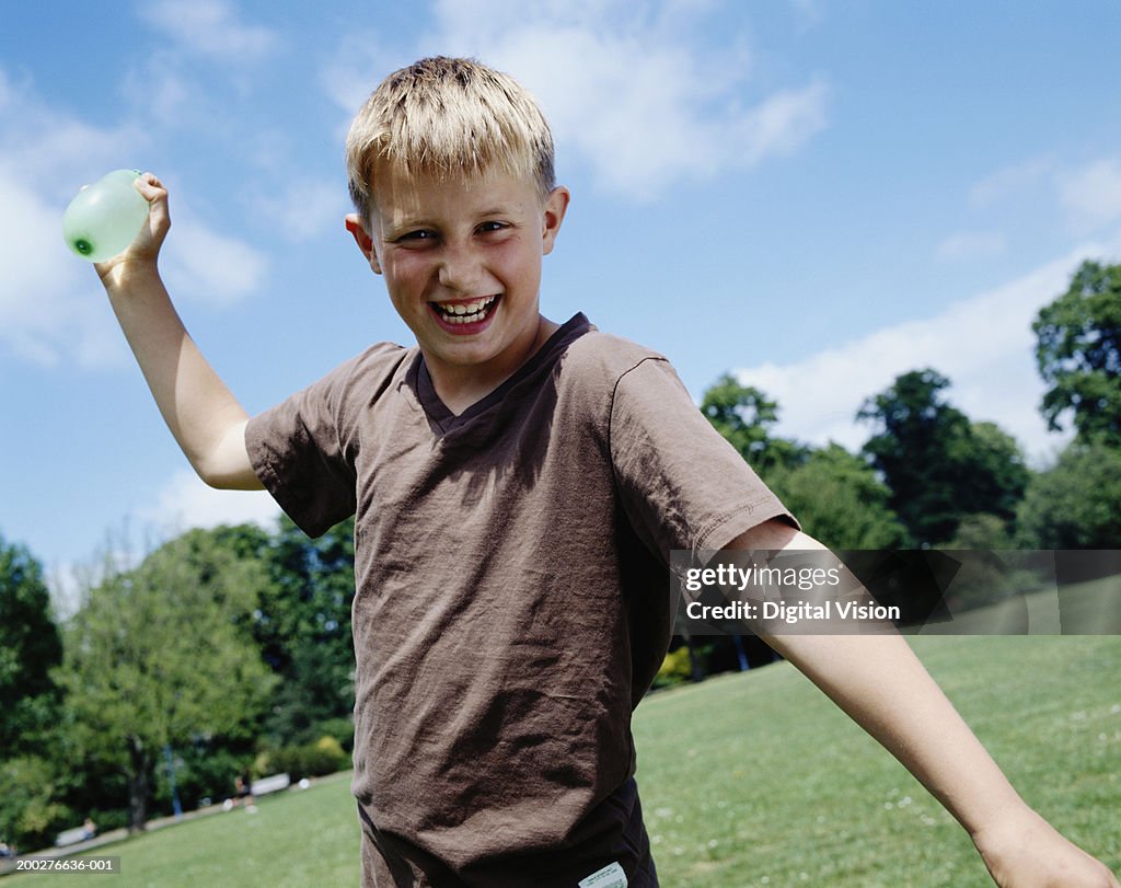 Boy (9-11) in park, aiming water bomb, smiling, portrait