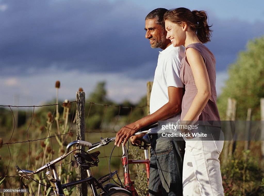 Couple with bicycles standing by fence, side view