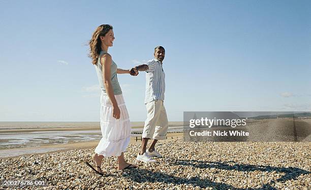 couple holding hands on pebble beach, laughing - blue skirt stockfoto's en -beelden