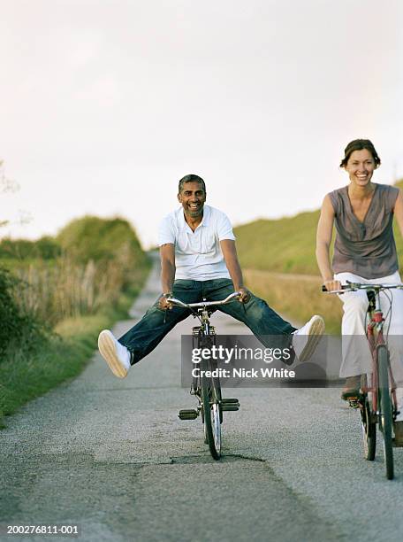 couple riding bicycles on path, man balancing with outstretched legs - mature indian couple stock-fotos und bilder