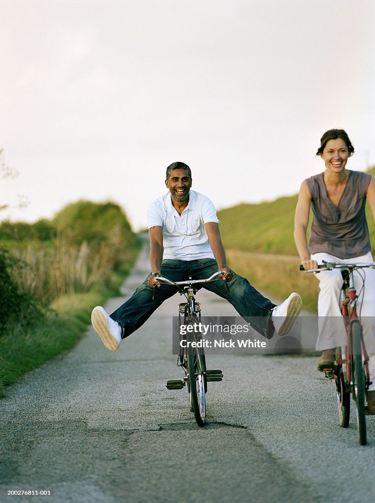 Couple riding bicycles on path, man balancing with outstretched legs