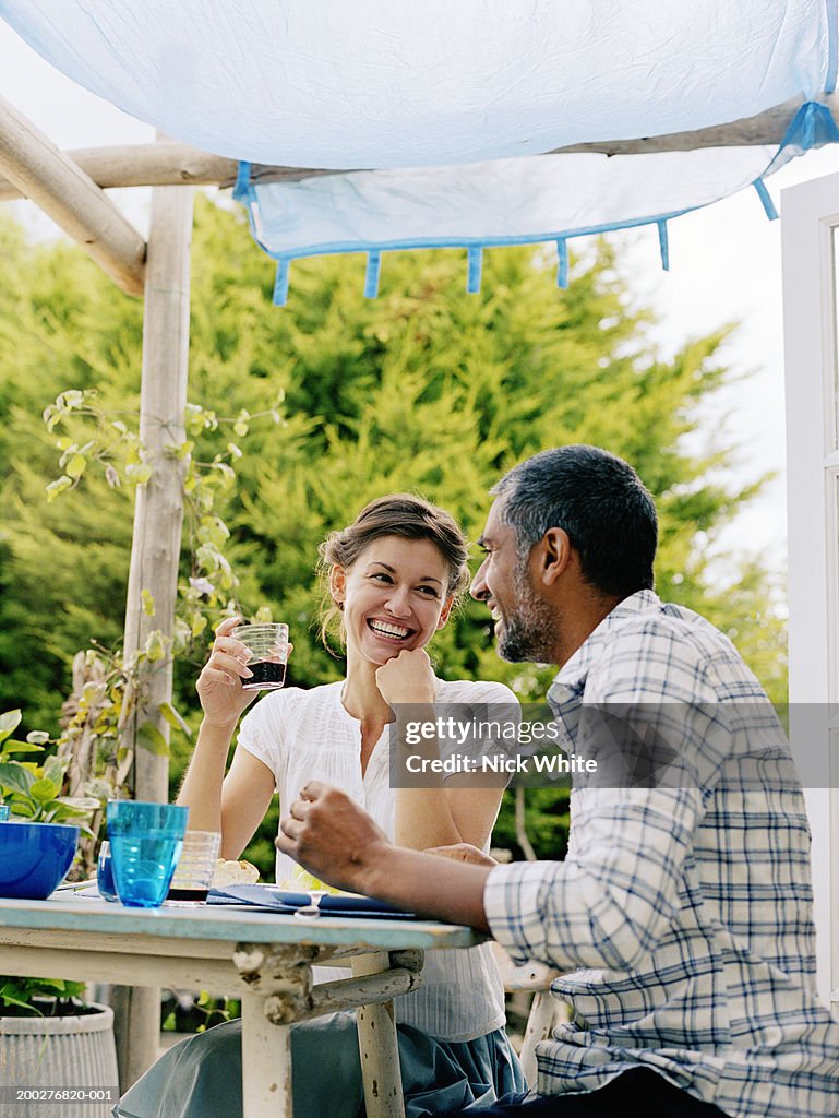 Couple dining outdoors, woman looking at man, both laughing