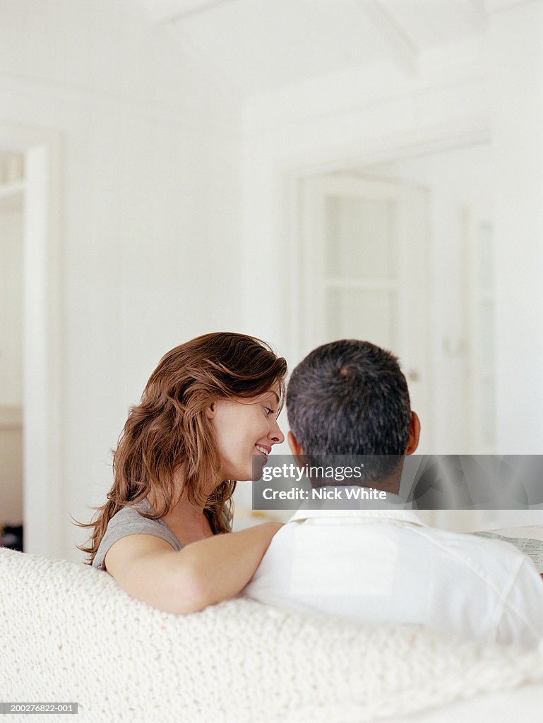 Couple relaxing on sofa, woman smiling, rear view