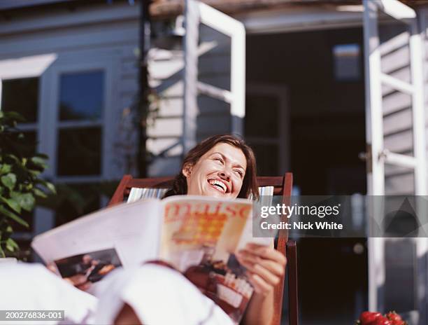 woman relaxing in deckchair holding magazine, leaning back laughing - magazines stockfoto's en -beelden