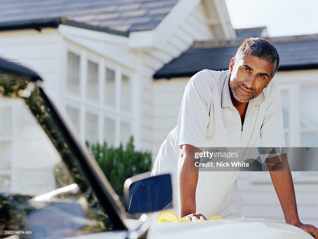 Man leaning on hood of car parked outside house, portrait
