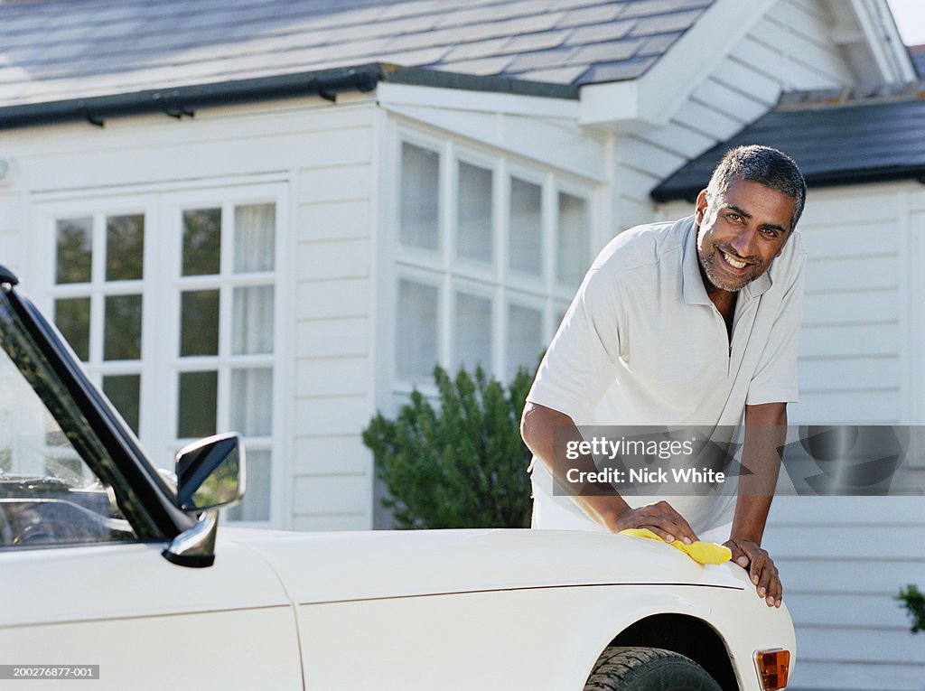 Man cleaning car parked outside house, smiling, portrait