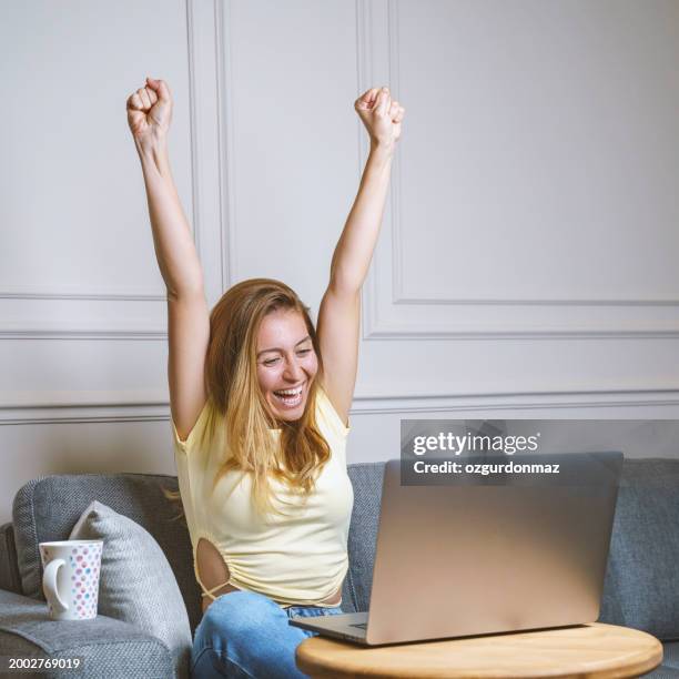 woman working from home online while using a laptop computer and celebrating with arms up - auction bid stock pictures, royalty-free photos & images