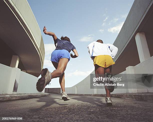 man and woman running up slope of multi-storey car park, rear view - sports car photos et images de collection