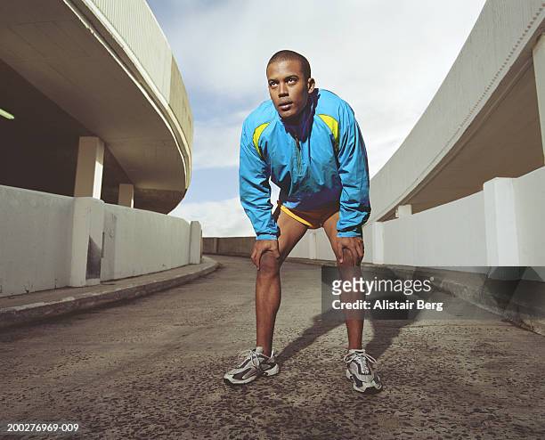young male runner on multi-storey car park slope, hands on knees - tracksuit jacket stock-fotos und bilder