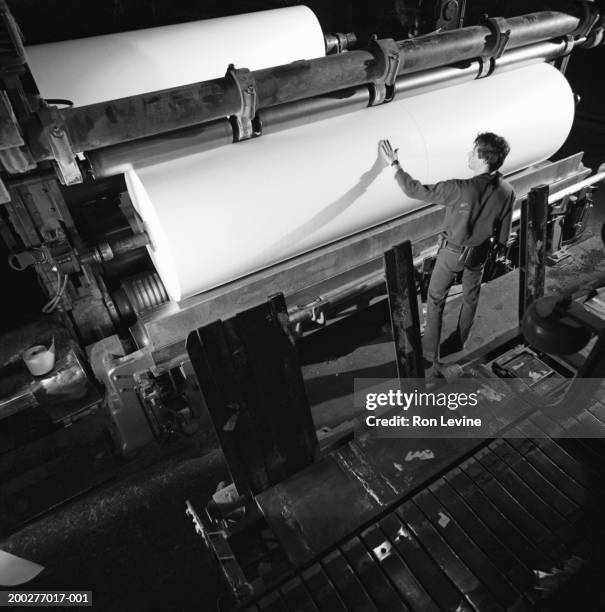 man inspecting roll of paper in mill, rear view (b&w) - paper industry stock-fotos und bilder