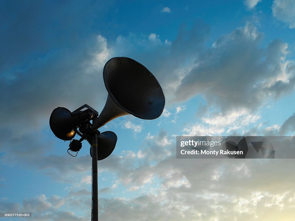 Loudspeakers mounted on pole under cloudy sky, low angle view