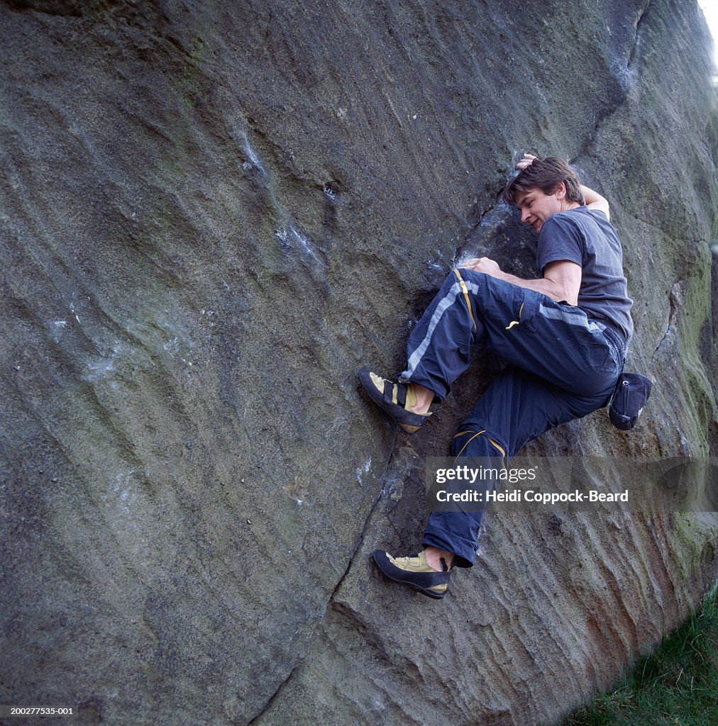 Man rock climbing along crack in rock wall, low angle view